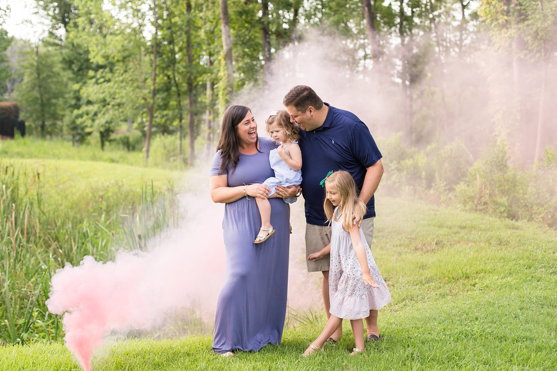 family of five smiling as pink smoke behind them reveals that their new baby will be a girl