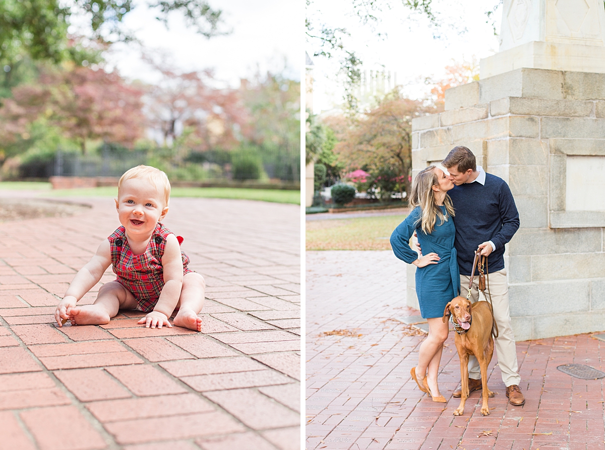 baby boy smiles sitting on the ground as parents kiss walking their dog