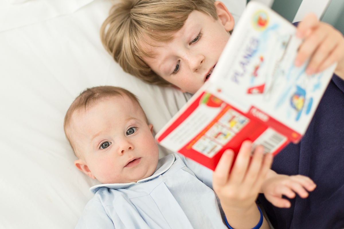 baby looks at book that big brother is reading in crib