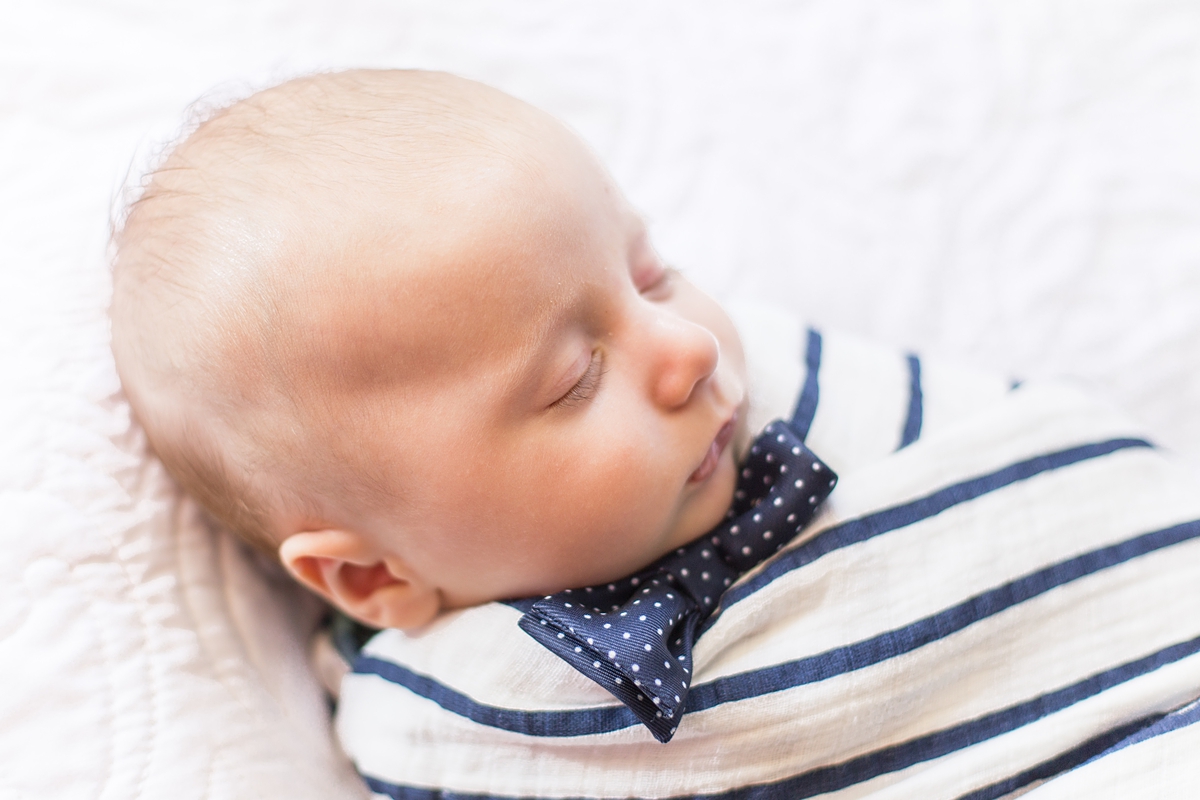 baby boy in navy blue bow tie sleeps swaddled in blanket