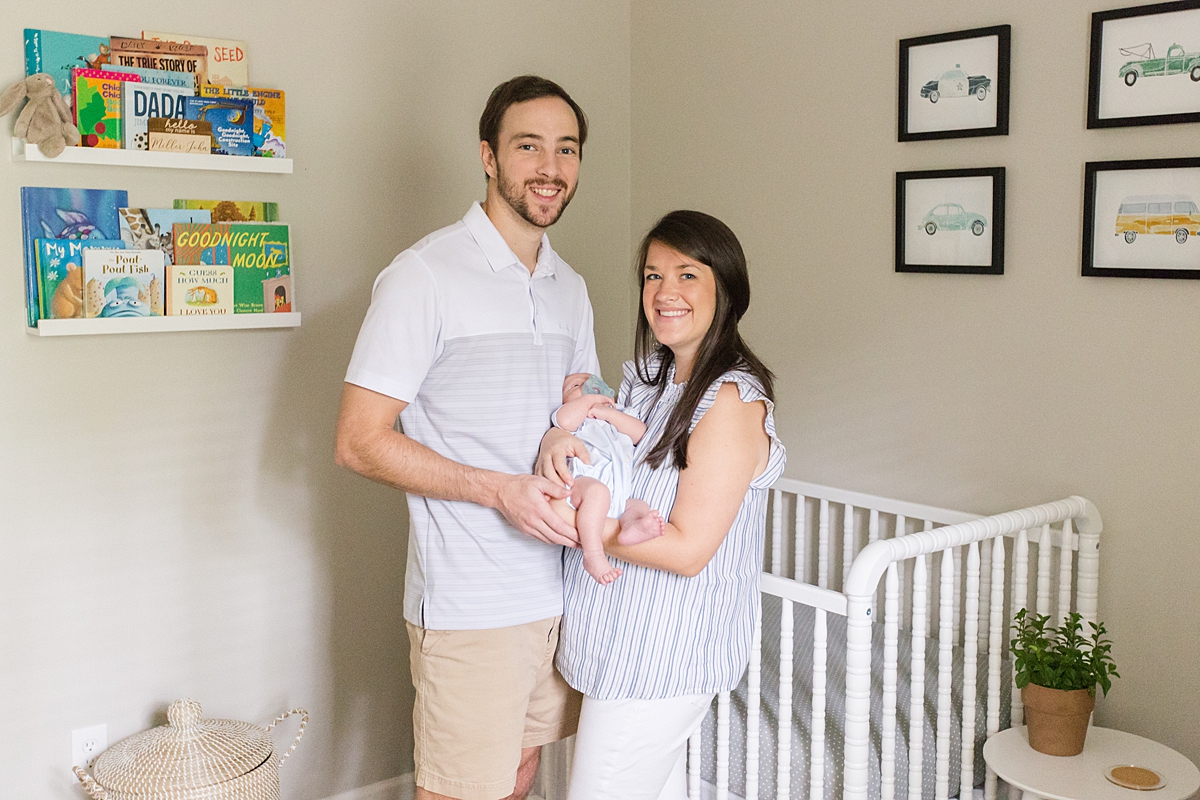 mom + dad hold their newborn son by crib in nursery during in-home lifestyle session in SC