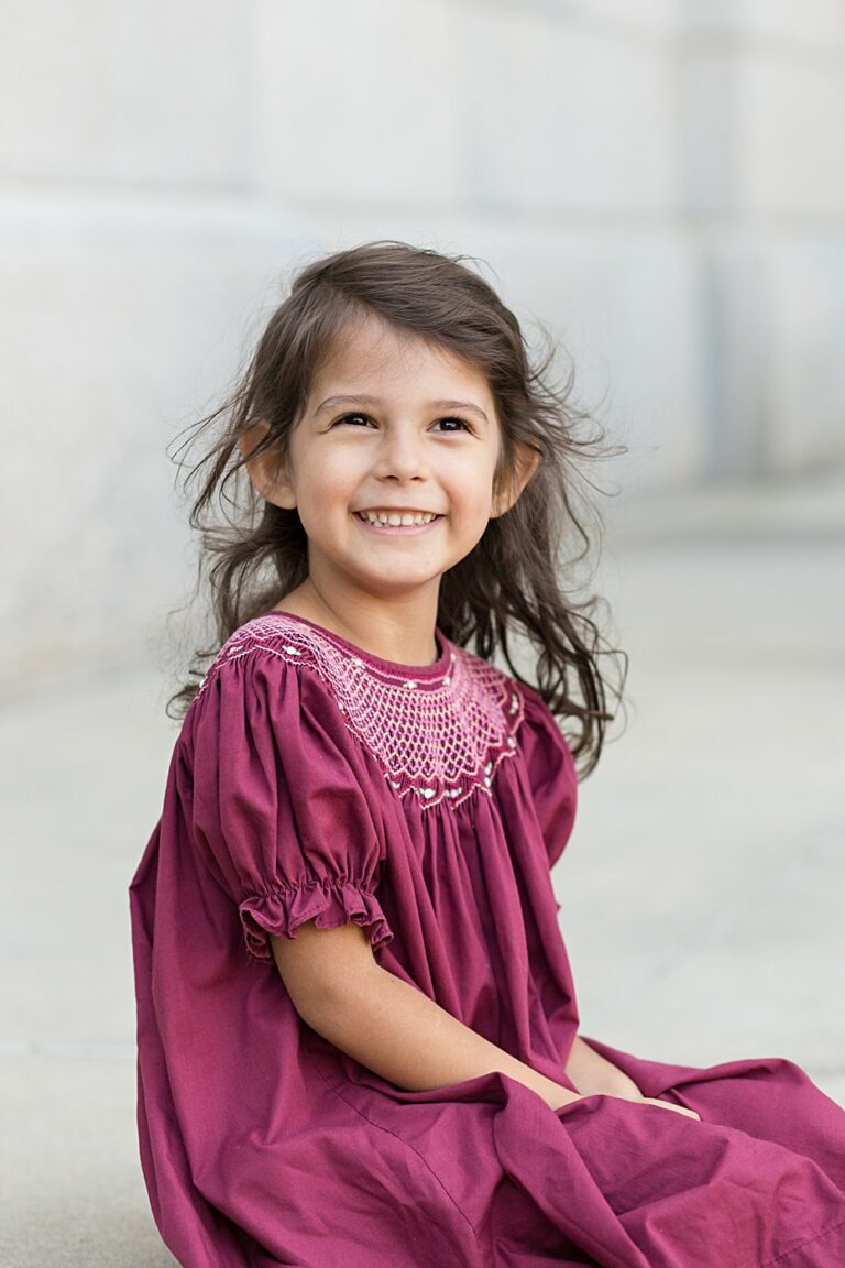 girl in maroon smocked dress sitting and smiling at camera